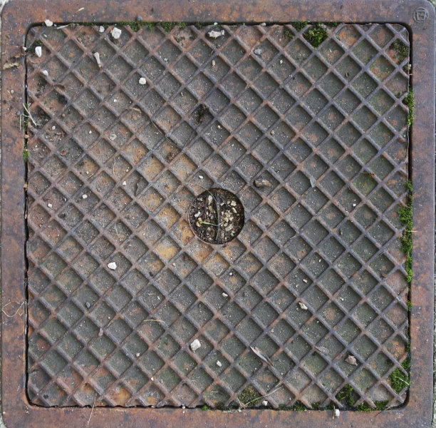 鸟瞰图上的一个矩形的锈蚀和肮脏的下水道盖覆盖着污垢，石头和绿色的苔藓，并加强了金属方形图案图片下载