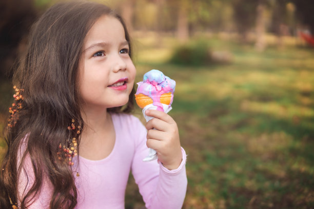 可爱的金发卷发女孩在公园里吃着美味的冰淇淋，儿童节的概念，复制空间图片下载
