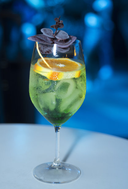 绿色鸡尾酒在一个高窄的玻璃杯里，配上一颗橘子。俱乐部的照明。宏观照片图片下载