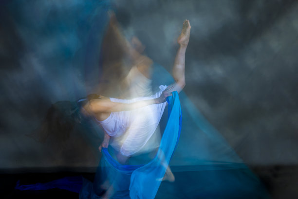 神秘的，模糊的舞蹈照片的成年妇女与浮动的蓝色织物。图片下载
