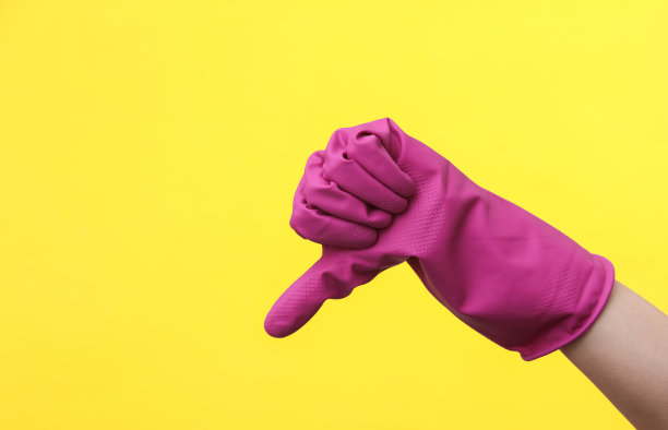 戴着紫色橡胶清洁手套的手在黄色背景上显示拇指朝下。房屋清洁和家务管理理念图片下载