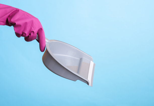 手在紫色橡胶清洁手套持有勺在蓝色背景。房屋清洁和家务管理理念图片下载