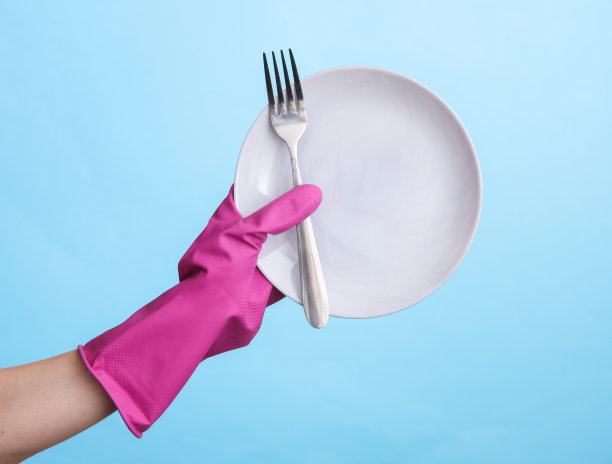 手在紫色橡胶清洁手套握住盘子和叉子在蓝色背景。图片下载