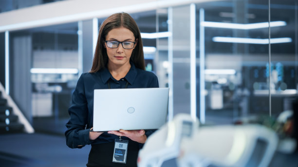 一个漂亮的白人女性的肖像，穿着漂亮的工作服，戴着眼镜，使用笔记本电脑。女商人，信息技术经理，机器人工程专家。图片下载