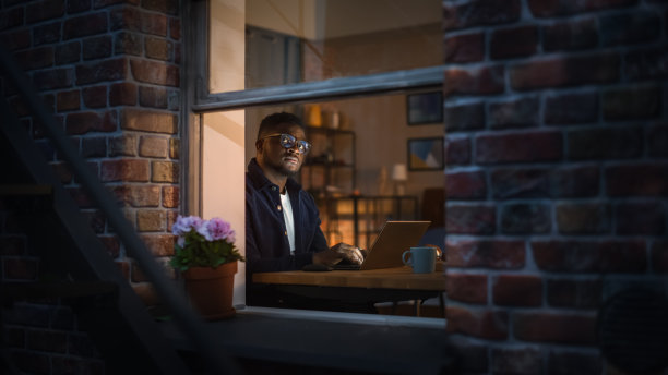 黑人富有成效的年轻人在卧室书桌上用笔记本电脑工作的肖像。商人制定电子商务战略和头脑风暴。他在思考和打字。窗外景色图片下载