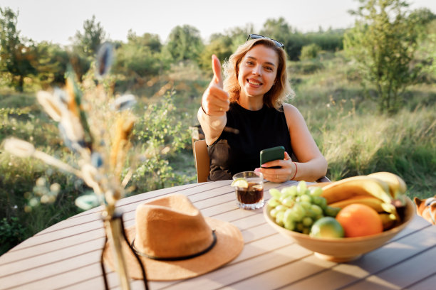 快乐的女人自由职业者使用电话和喝鸡尾酒电话，而放松在舒适的豪华帐篷在阳光明媚的日子。豪华户外露营帐篷，适合夏季度假度假。生活方式的概念图片下载