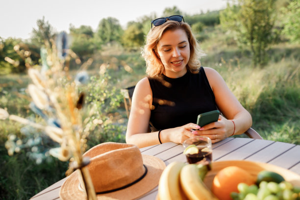 快乐的女人自由职业者使用电话和喝鸡尾酒电话，而放松在舒适的豪华帐篷在阳光明媚的日子。豪华户外露营帐篷，适合夏季度假度假。生活方式的概念图片下载