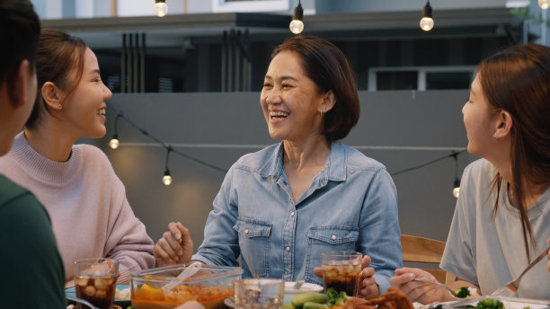 中年妈妈在饭桌上谈笑风生。亚洲人，成年人，老人，妈妈，享受食物，欢乐，欢笑，快乐时光，在舒适的野餐，温暖的时间，晚上，晚餐，周末。年轻的老年妇女放松退休。图片下载