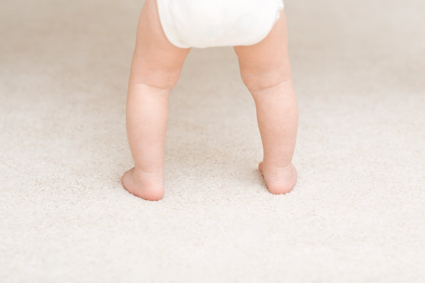 Baby barefoot standing on light soft сarpet at home room. Closeup. First steps. Back view. Infant development.图片下载