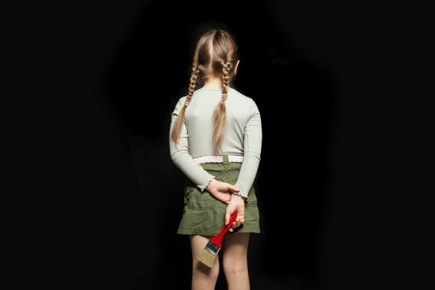 小女孩背对着黑板，拿着画笔站在黑板的背景上图片下载