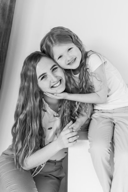 年轻快乐的妈妈带着孩子女儿孤立在白色背景的工作室里。滑稽的父母在家里的墙上拥抱女孩。一家人搬进新居，心情愉快。母亲拥抱孩子。黑白照片。图片下载