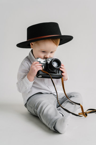 国际摄影师日。有趣的孩子拿着复古的老式相机孤立在白墙上。戴着帽子的孩子坐在地板上玩照相机。孩子们的工作室肖像。模型。关闭了。图片下载