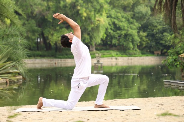 清晨，一个英俊的年轻人在公园的绿色宁静的环境中锻炼和做瑜伽，以保持健康的生活方式。图片下载