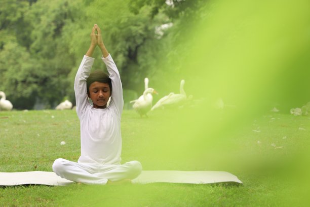 快乐的印度男孩早上坐在公园的瑜伽垫上做瑜伽。图片下载