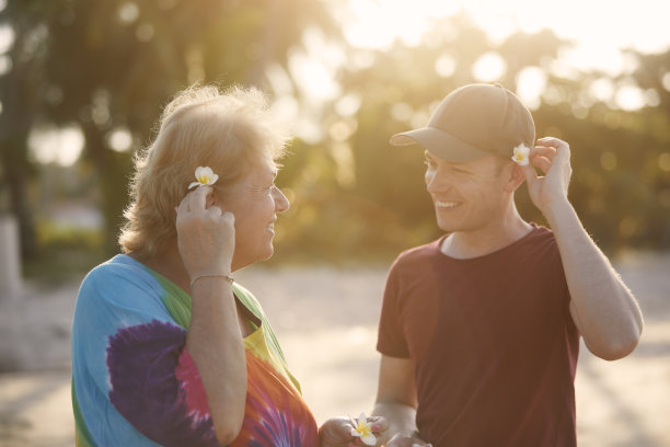 快乐的老年妇女和她成年的儿子在日落的海滩上的画像图片下载