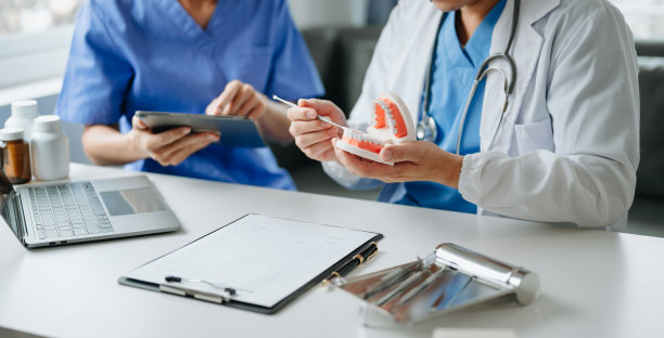 牙科诊所专业牙科诊所的牙医坐在桌子上与颌骨样本牙齿模型和平板电脑和笔记本电脑工作。医生工作图片下载