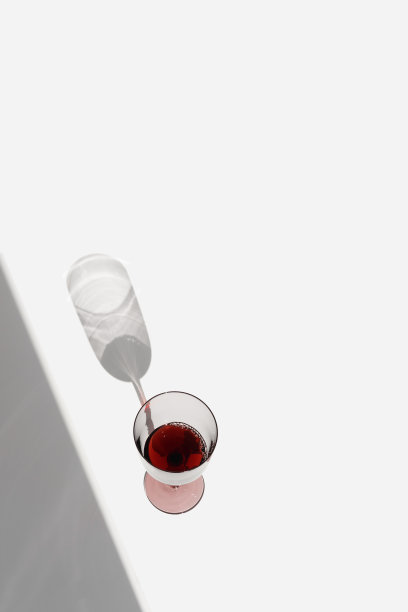 极简静物与一杯干红葡萄酒与阳光的阴影，夏天平躺。一个高大的红酒杯，在白色的背景上喝酒，复制空间，时尚唯美的照片图片下载