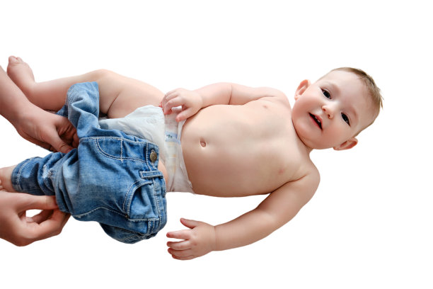 一位母亲为一个孤立在白色背景上的小男孩穿上牛仔裤。妈妈给快乐的孩子穿上衣服。9个月大的孩子图片下载