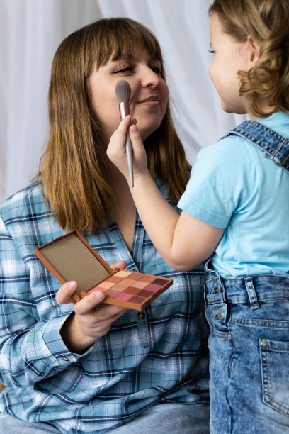 漂亮可爱的小女孩正在用眼影板和眼影刷给妈妈化妆。优质的家庭时光，享受家庭生活，为人母。妇女节或母亲节庆祝活动，一起玩乐图片下载