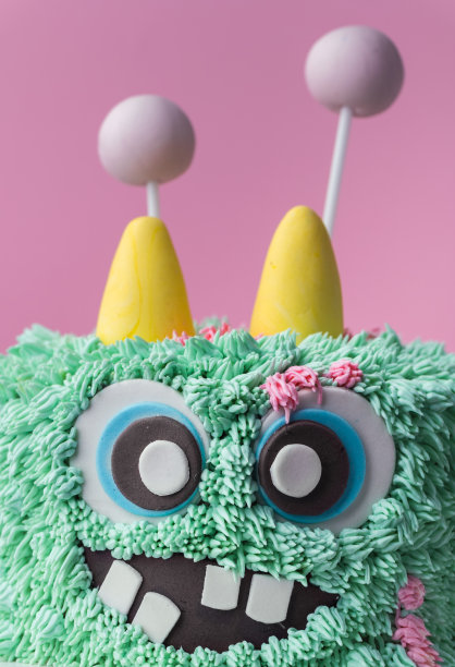 粉红色背景上的怪物主题蛋糕。有趣的生日蛋糕，上面有绿松石松软的奶油芝士糖霜。带有可食用皮毛的恐怖怪物糕点。万圣节派对快乐图片下载