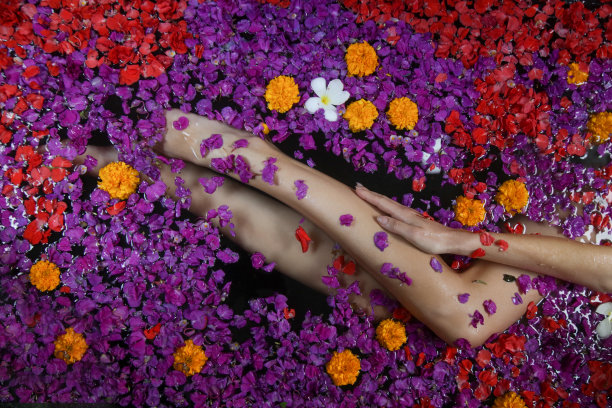 年轻女子在满是花瓣的浴缸里洗澡，收腿，水疗周末，健康，身体护理和美容概念图片下载