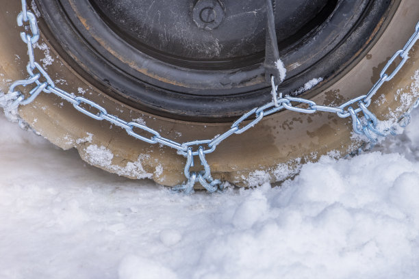 车轮在雪地与安全和防滑链。装载机或拖拉机，车轮上有链条特写。冬季行车安全图片下载