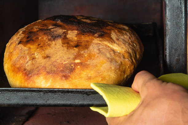 在家里用老式烤箱烤面包。面包师的手拿出一个托盘，上面放着刚烤好的面包。乌克兰传统食物。图片下载