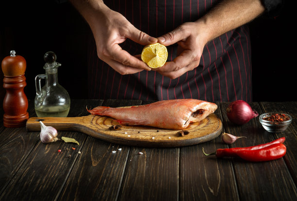 厨师把新鲜的柠檬汁加到生鲈鱼里。餐厅或酒店的美味红鱼午餐的概念。图片下载