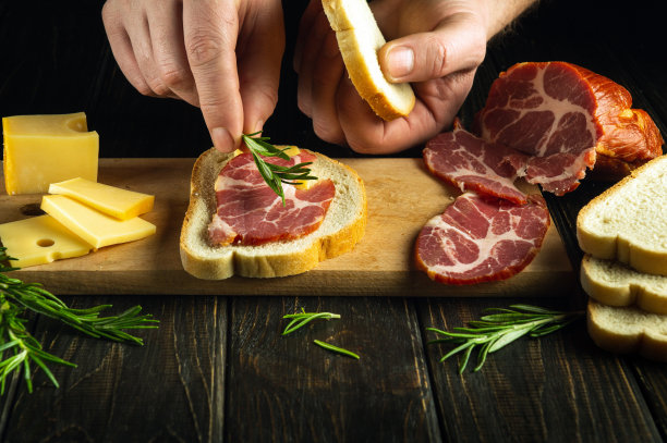 厨师在厨房的桌子上做了露面火腿和奶酪小吃式的三明治。菜谱或菜单的黑暗空间。美味的快餐点子。图片下载