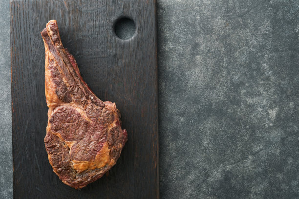 Tomahawk牛排。切成薄片的烤战斧式牛排，配上烤过的圣女果、香草和盐。准备烧烤。俯视图和复制空间。图片下载