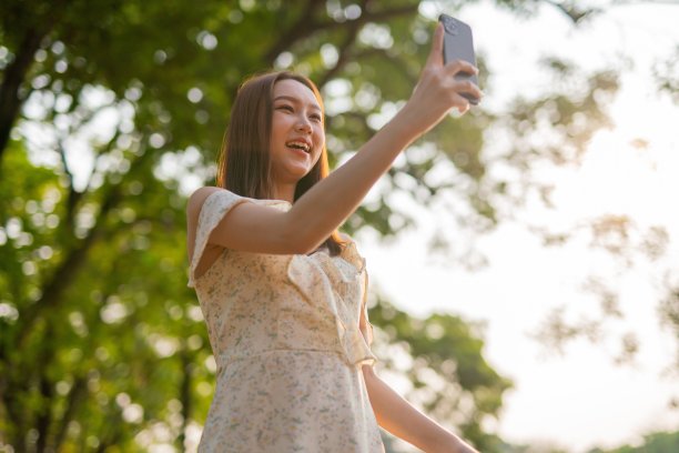 年轻的亚洲女子在公园用手机自拍。在郁郁葱葱的绿色森林里，美女视频通话图片下载