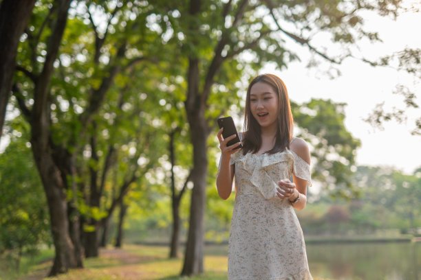 年轻的亚洲女子在公园里使用手机应用程序。美丽的女人在郁郁葱葱的绿色森林里查看手机上的应用程序图片下载