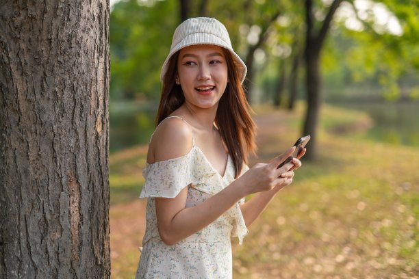 年轻的亚洲女子在公园里使用手机应用程序。美丽的女人在郁郁葱葱的绿色森林里查看手机上的应用程序图片下载