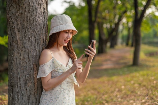 年轻的亚洲女子在公园里使用手机应用程序。美丽的女人在郁郁葱葱的绿色森林里查看手机上的应用程序图片下载