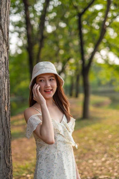 年轻的亚洲女人在公园里用手机。一个美丽的女人在郁郁葱葱的森林里打电话聊天图片下载