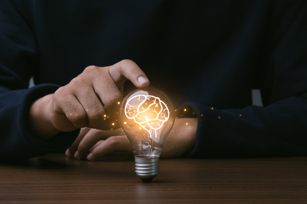 创新思维理念为技术理念。人的手触摸灯泡与橙色发光和大脑的图标。概念的概念。图片下载