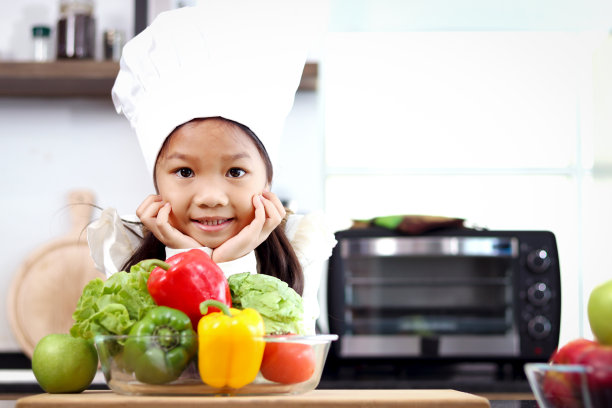 亚洲女孩穿着围裙，戴着厨师帽，站在厨房柜台前，拿着五颜六色的新鲜蔬菜沙拉食品配料，可爱的小厨师孩子准备烹饪健康食品。图片下载