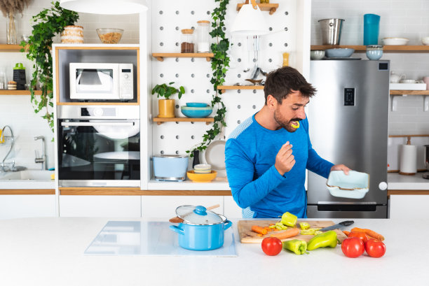 微笑的年轻胡须运动男人在现代厨房里做沙拉，切新鲜蔬菜，快乐满足的男性准备素食小吃，晚餐或聚会的食物，享受闲暇时间，爱好图片下载