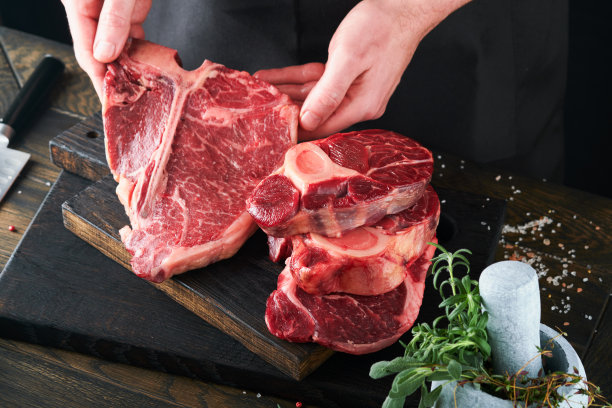 牛排、牛肉、肉。厨师在切牛排。他的手拿着生牛排战斧在黑色背景的质朴木制砧板上。烹饪，食谱和饮食观念。有选择性的重点。图片下载