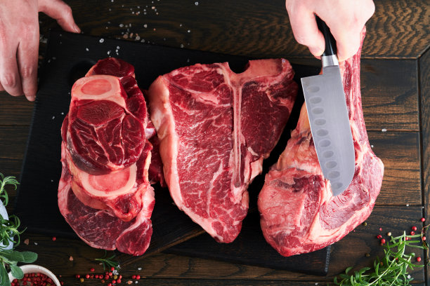 牛排、牛肉、肉。厨师在切牛排。他的手拿着生牛排战斧在黑色背景的质朴木制砧板上。烹饪，食谱和饮食观念。有选择性的重点。图片下载
