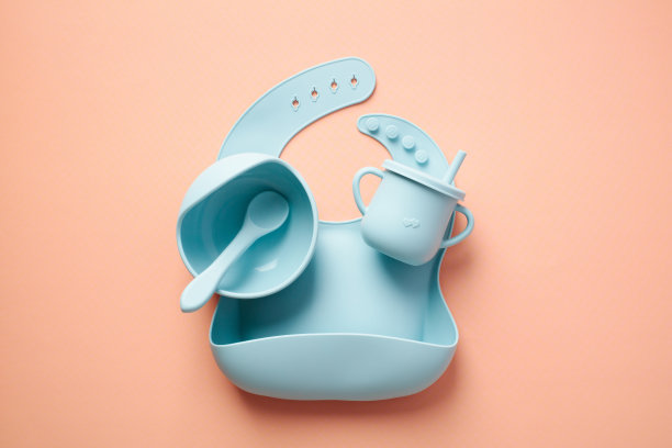 婴儿喂养套装。硅胶围嘴，碗和吸管杯的颜色背景。图片下载