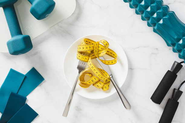 用餐具，天平，跳绳，滚轮，橡皮筋，大理石背景上的哑铃测量盘上的卷尺。减肥，饮食观念。图片下载