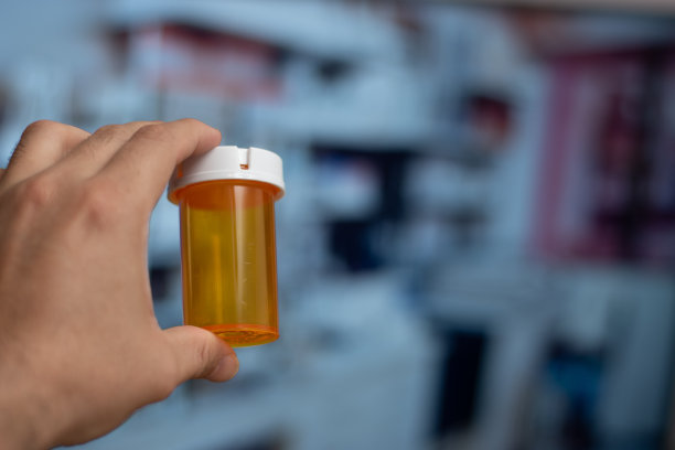 在实验室背景中，手拿着一个空的橙色药瓶图片下载