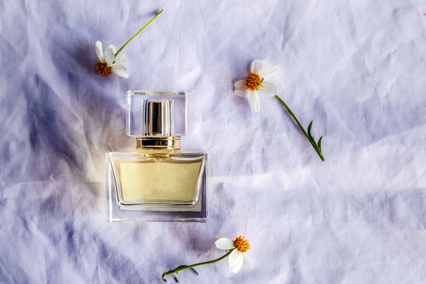 金色香水和小香水瓶与白布背景上的白花，俯视图图片下载