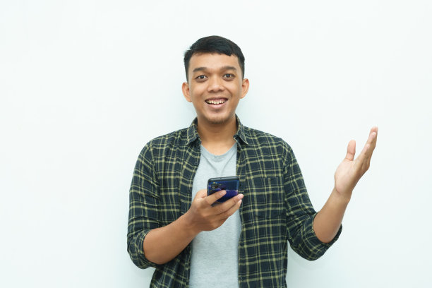 年轻的亚洲男子微笑着拿着智能手机，另一只手指着左边图片下载