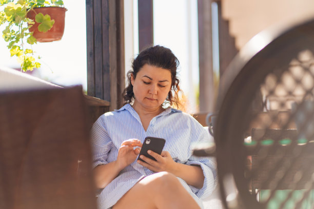 深色头发的中年女人在房子的阳台上用电话喝咖啡图片下载