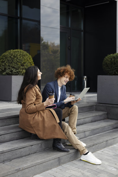 微笑迷人的男人和女人坐在现代化办公室附近的楼梯上，用笔记本电脑，喝咖啡图片下载