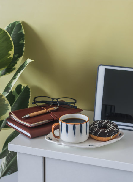 家庭办公室的咖啡休息时间——办公桌上放着笔记本、平板电脑和文具，上面放着咖啡和巧克力糖霜的甜甜圈图片下载
