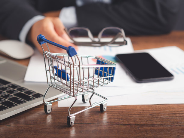 一张木桌上放着一辆迷你购物车，一个男人坐在办公室里拿着眼镜。图片下载