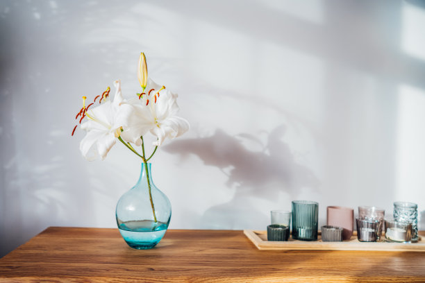 现代简约的斯堪的纳维亚风格的室内设计，白色的海报模型，蜡烛和白色的百合，在阳光下的木制控制台的花瓶和灰色墙壁上的家庭植物阴影。有选择性的重点。图片下载